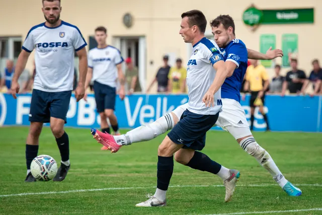 Fotbalista v bílém dresu zakončuje střelou v plném běhu